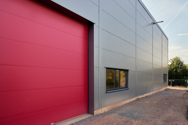 Ein Himbeerrotes Sektionaltor vor einer Stahlhalle - eine farbenfrohe und ansprechende Option für den Eingangsbereich.